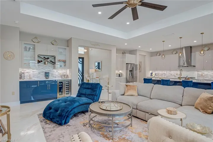 Living room featuring a raised ceiling, beverage cooler, a bar, and a ceiling fan