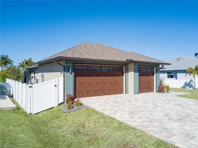 View of front facade with stucco siding, decorative driveway, roof with shingles, and a gate