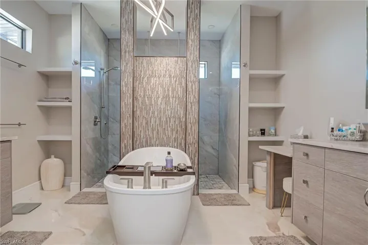 Bathroom featuring vanity, built in shelves, a marble finish shower, and a freestanding bath