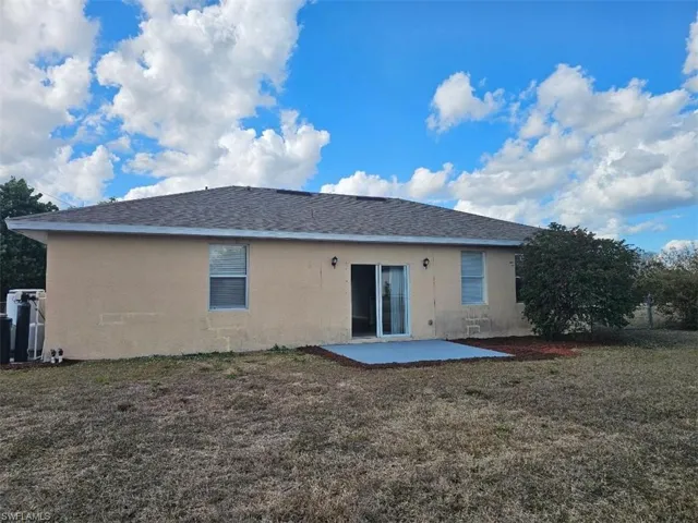 Back of house featuring a patio, stucco siding, a lawn, and roof with shingles