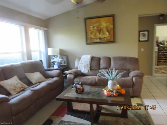Living area with lofted ceiling, tile patterned flooring, and ceiling fan
