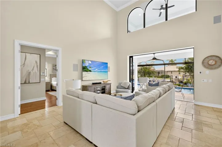 Living room featuring ceiling fan, stone tile floors, a towering ceiling, and ornamental molding