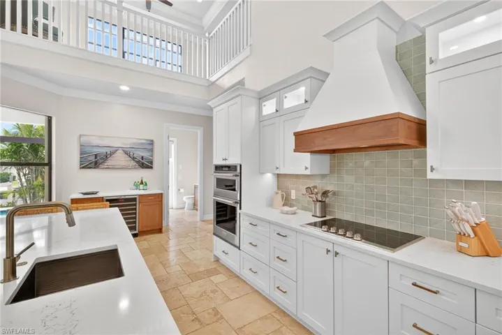 Kitchen featuring a high ceiling, stone tile flooring, custom exhaust hood, white cabinetry, and tasteful backsplash