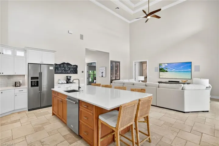 Kitchen featuring a high ceiling, stone tile flooring, ornamental molding, stainless steel appliances, and a kitchen bar
