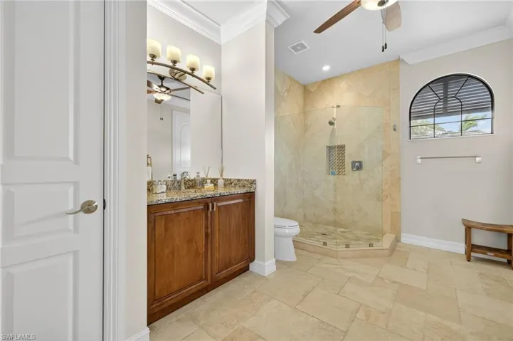 Full bath with ceiling fan, ornamental molding, a stall shower, vanity, and stone tile flooring