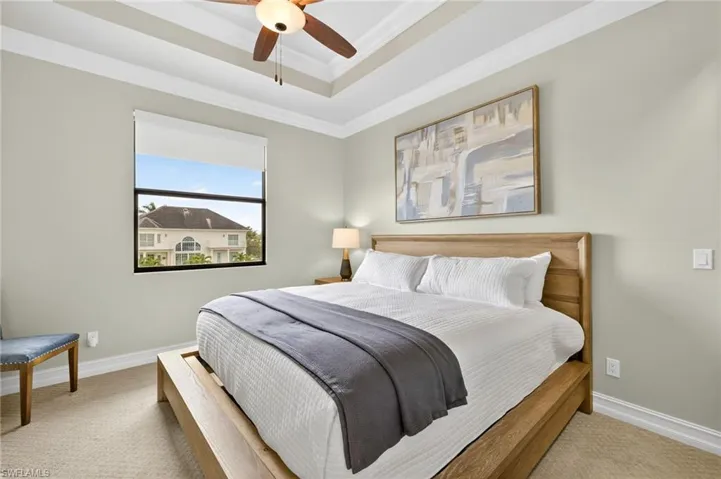 Carpeted bedroom with a raised ceiling, crown molding, and a ceiling fan