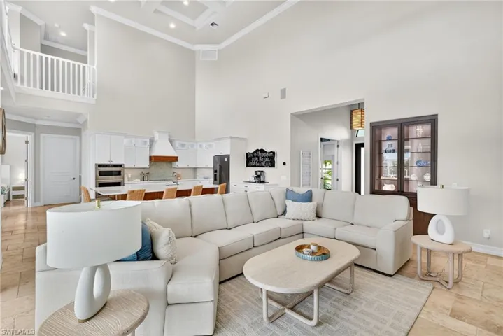 Living room featuring a high ceiling, ornamental molding, recessed lighting, stone tile floors, and beam ceiling