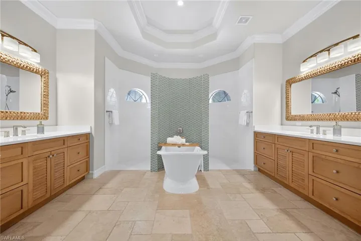 Bathroom with a walk in shower, two vanities, a raised ceiling, and crown molding