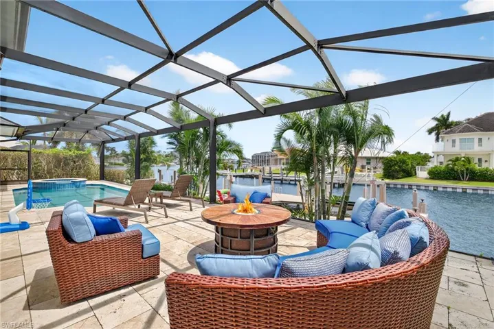 View of patio with a pool with connected hot tub, a water view, a lanai, and an outdoor living space with a fire pit
