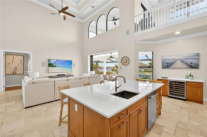 Kitchen with ceiling fan, a towering ceiling, crown molding, wine cooler, and stone tile floors