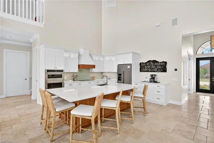 Kitchen with a towering ceiling, stone tile flooring, light countertops, custom exhaust hood, and stainless steel appliances