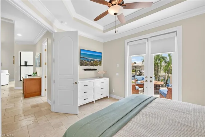 Bedroom featuring french doors, access to exterior, crown molding, a raised ceiling, and stone tile flooring