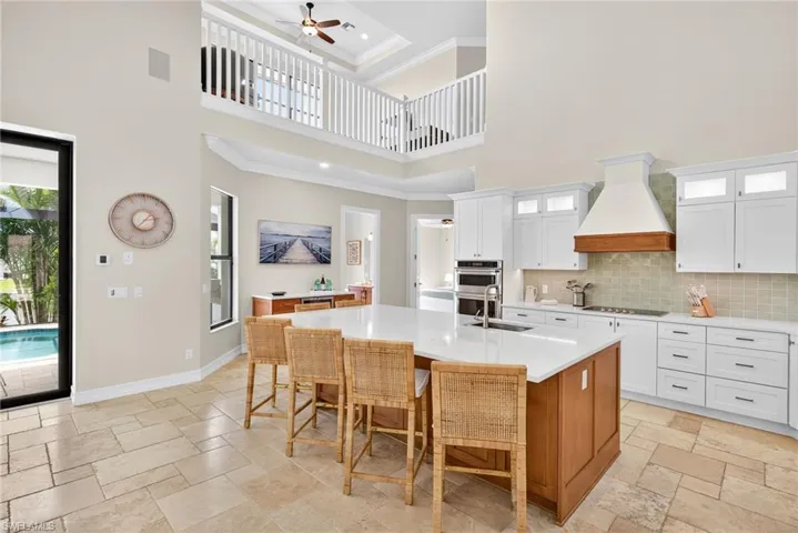 Kitchen with a towering ceiling, stone tile flooring, custom range hood, light countertops, and crown molding