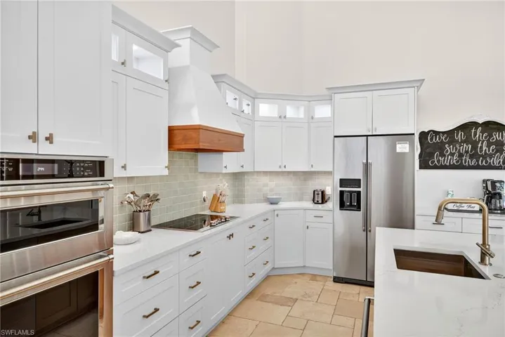 Kitchen featuring stainless steel appliances, tasteful backsplash, white cabinetry, and light stone counters