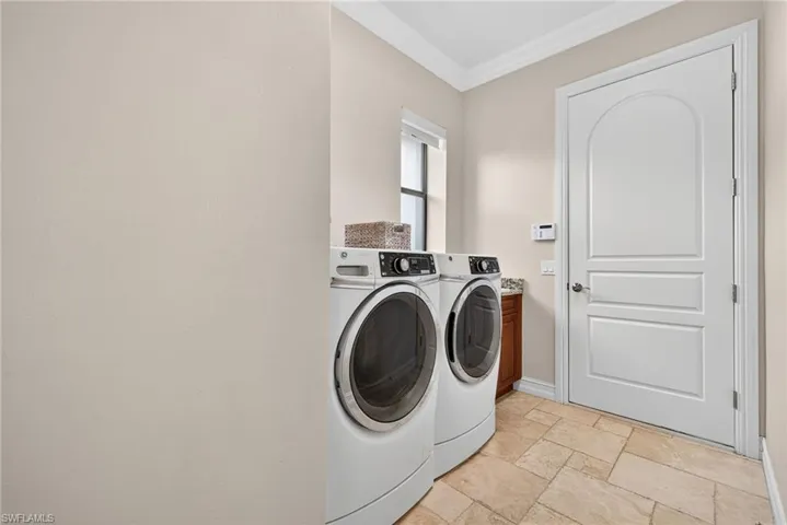 Laundry area featuring independent washer and dryer, stone tile floors, ornamental molding, and cabinet space