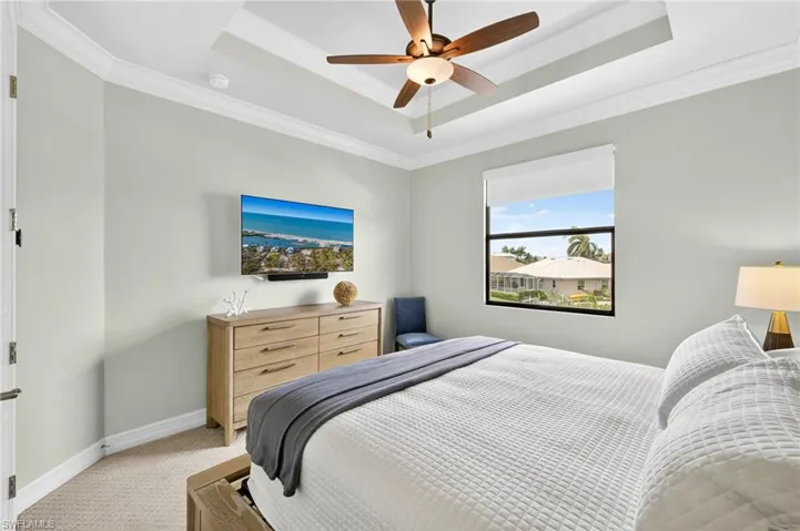 Bedroom with ornamental molding, light carpet, a raised ceiling, and ceiling fan