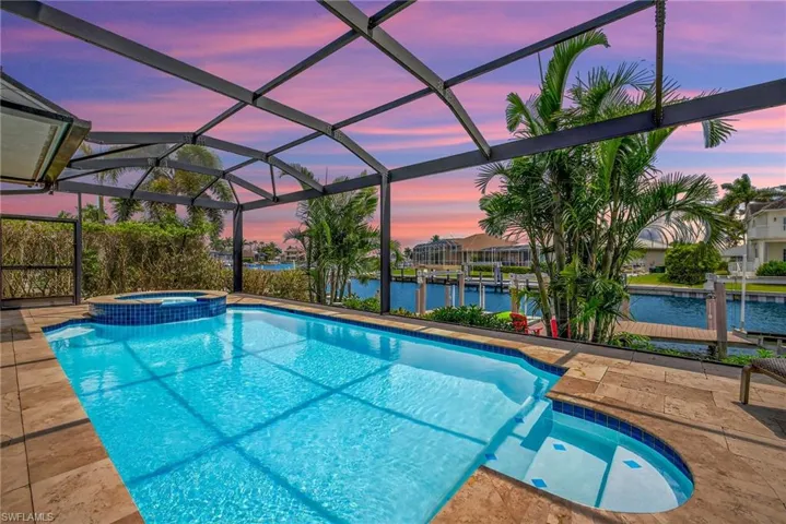 View of swimming pool featuring a water view, a pool with connected hot tub, glass enclosure, and a patio