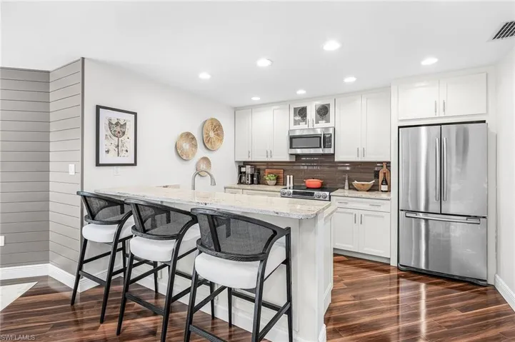 Updated kitchen with granite countertops, appliances with stainless steel finishes, a breakfast bar area, glass insert cabinets, and recessed lighting