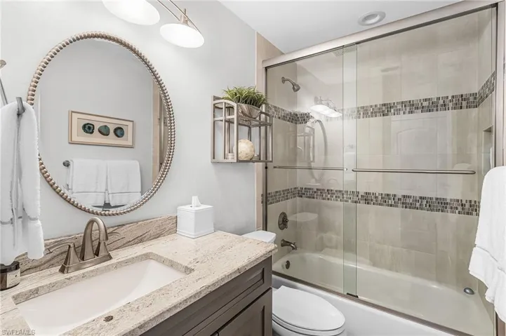 Updated bathroom with vanity and combined tub/shower with accent tiles and glass door.