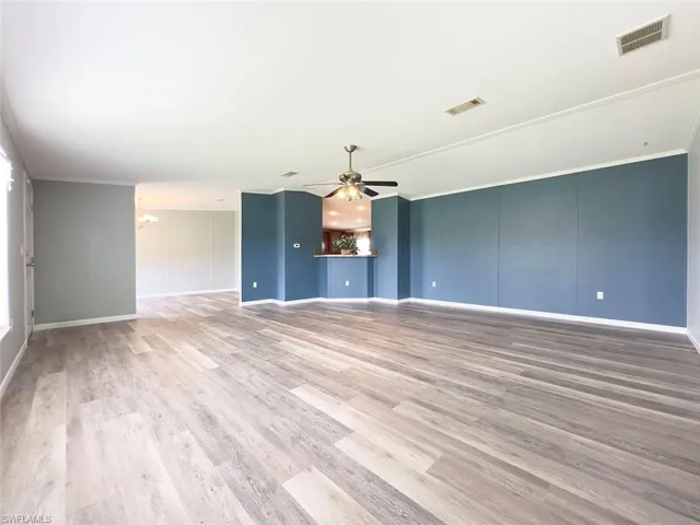 Unfurnished living room with crown molding, light wood-type flooring, and ceiling fan with notable chandelier