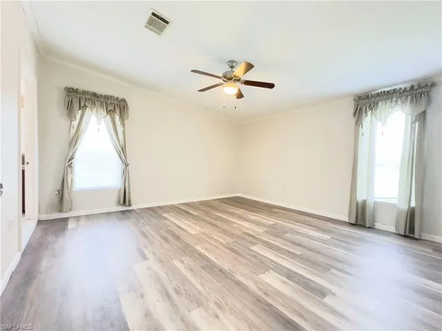 Empty room featuring a healthy amount of sunlight, wood-type flooring, crown molding, and ceiling fan