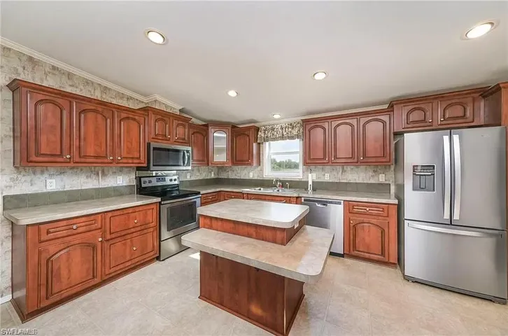 Kitchen with stainless steel appliances, crown molding, a kitchen island, and light tile floors
