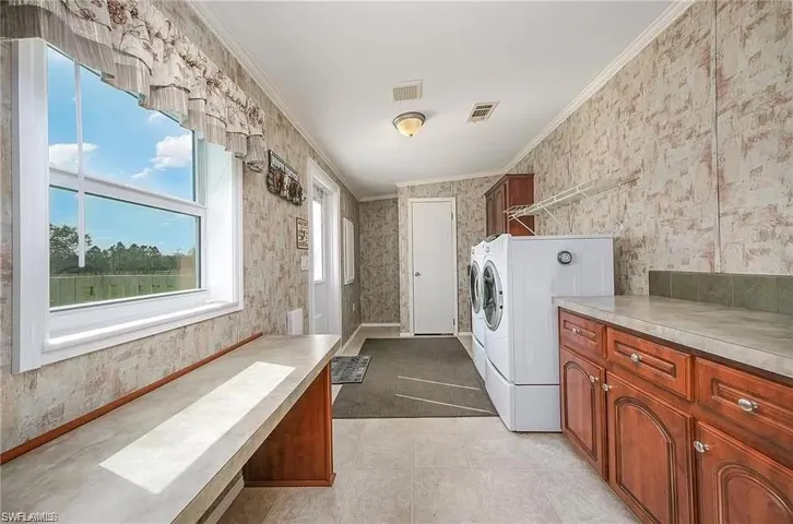 Laundry area with washer and dryer, cabinets, ornamental molding, and light tile floors