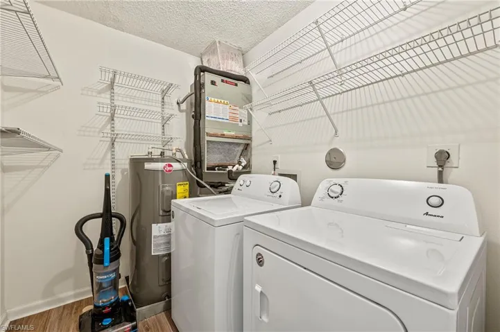 Laundry room featuring a textured ceiling, water heater, wood finished floors, washer and dryer, and heating unit