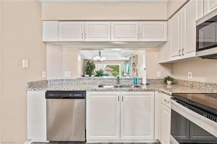 Kitchen featuring white cabinetry, stainless steel appliances, light stone countertops, and a chandelier