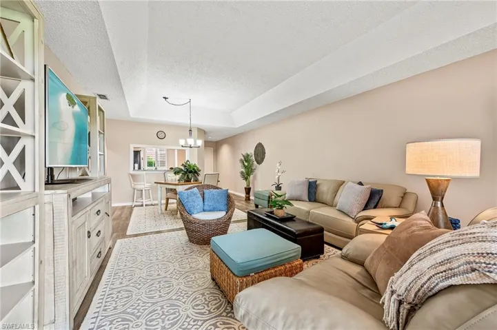 Living room featuring a tray ceiling, a chandelier, wood finished floors, and a textured ceiling
