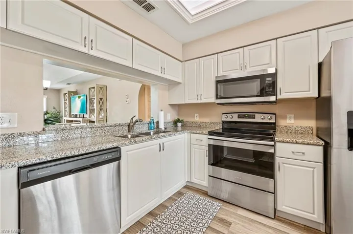 Kitchen with stainless steel appliances, white cabinetry, light stone counters, light wood-style floors, and a skylight