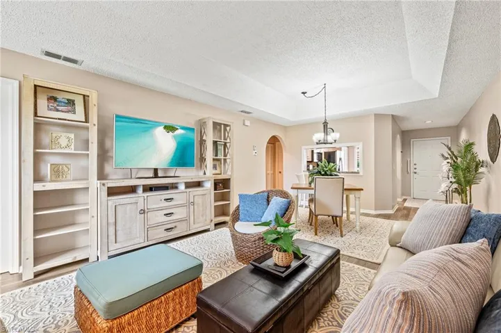 Living room featuring arched walkways, a textured ceiling, a chandelier, a raised ceiling, and wood finished floors
