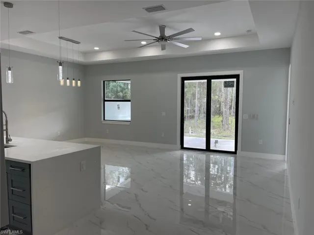 Unfurnished living room featuring a raised ceiling, ceiling fan, and a healthy amount of sunlight