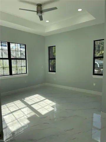 Empty room featuring a tray ceiling, ceiling fan, and a healthy amount of sunlight