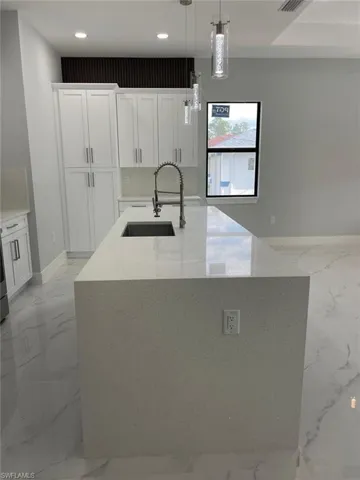 Kitchen with decorative light fixtures, sink, white cabinetry, and an island with sink