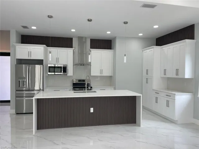 Kitchen with wall chimney range hood, sink, appliances with stainless steel finishes, decorative light fixtures, and white cabinetry