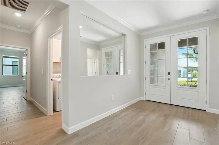 Doorway with ornamental molding, french doors, wood finished floors, and washer / clothes dryer