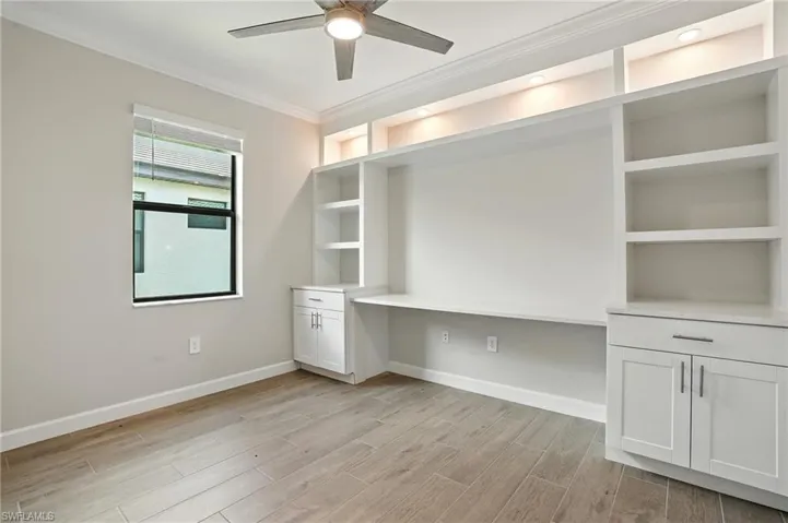 Unfurnished office featuring crown molding, wood tiled floors, built in desk, and a ceiling fan
