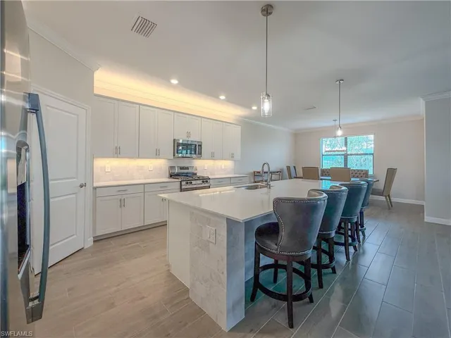 Kitchen featuring decorative light fixtures, crown molding, stainless steel appliances, wood tiled floors, and an island with sink