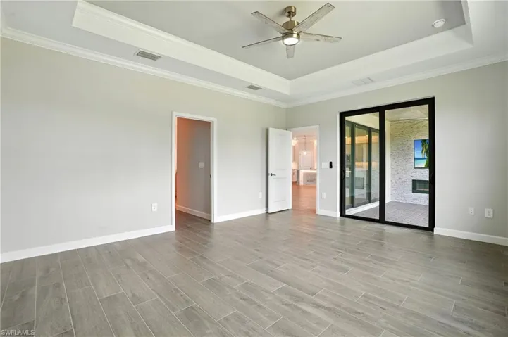 Empty room with a raised ceiling, ornamental molding, light wood-style floors, and ceiling fan