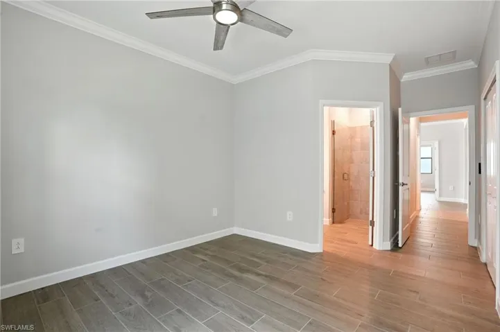 Unfurnished bedroom with ornamental molding, wood tiled floors, ceiling fan, and connected bathroom