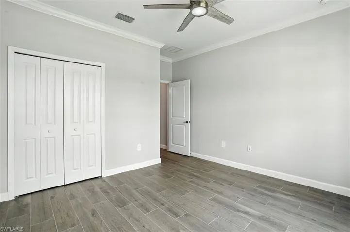 Unfurnished bedroom with ornamental molding, a ceiling fan, a closet, and wood finished floors