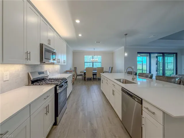 Kitchen featuring appliances with stainless steel finishes, crown molding, light stone counters, white cabinetry, and decorative light fixtures