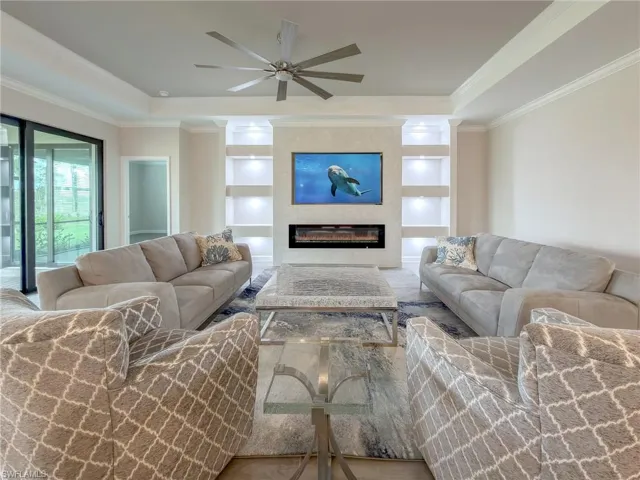 Living room with built in shelves, a large fireplace, a ceiling fan, a raised ceiling, and crown molding