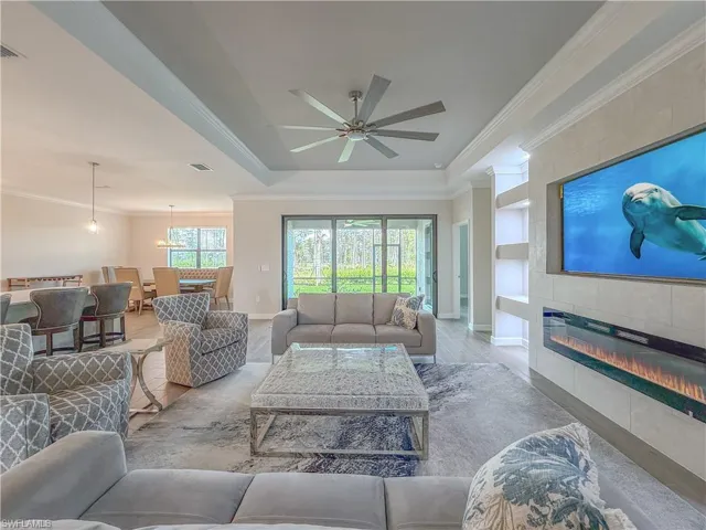 Living area with ornamental molding, built in features, a chandelier, a ceiling fan, and a tiled fireplace
