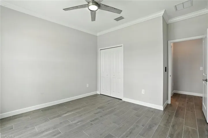 Unfurnished bedroom featuring crown molding, wood finish floors, a closet, and a ceiling fan