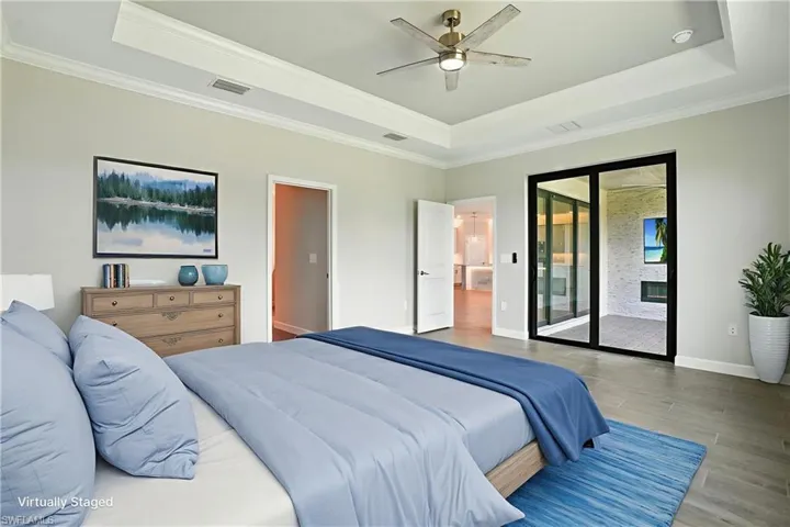 Bedroom with a raised ceiling, wood finished floors, ornamental molding, access to exterior, and ceiling fan