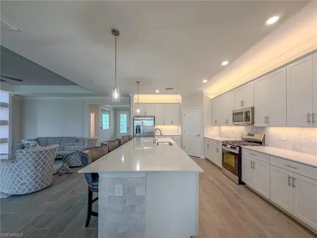 Kitchen with crown molding, appliances with stainless steel finishes, a kitchen breakfast bar, wood finish floors, and pendant lighting