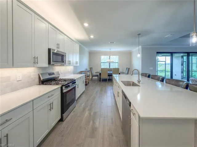 Kitchen with stainless steel appliances, a large island with sink, a breakfast bar, light wood-style flooring, and ornamental molding