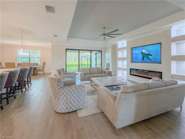 Living area with built in features, a raised ceiling, a fireplace, ornamental molding, and wood tiled floors